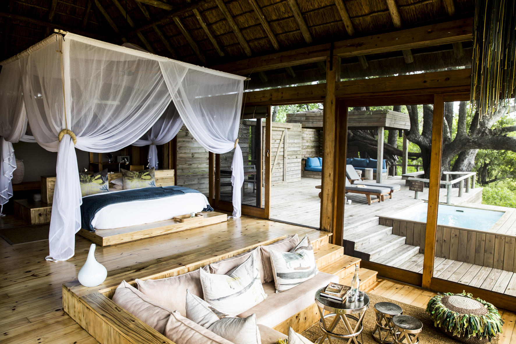 Interior of a luxury safari lodge with four-poster bed and private plunge pool deck